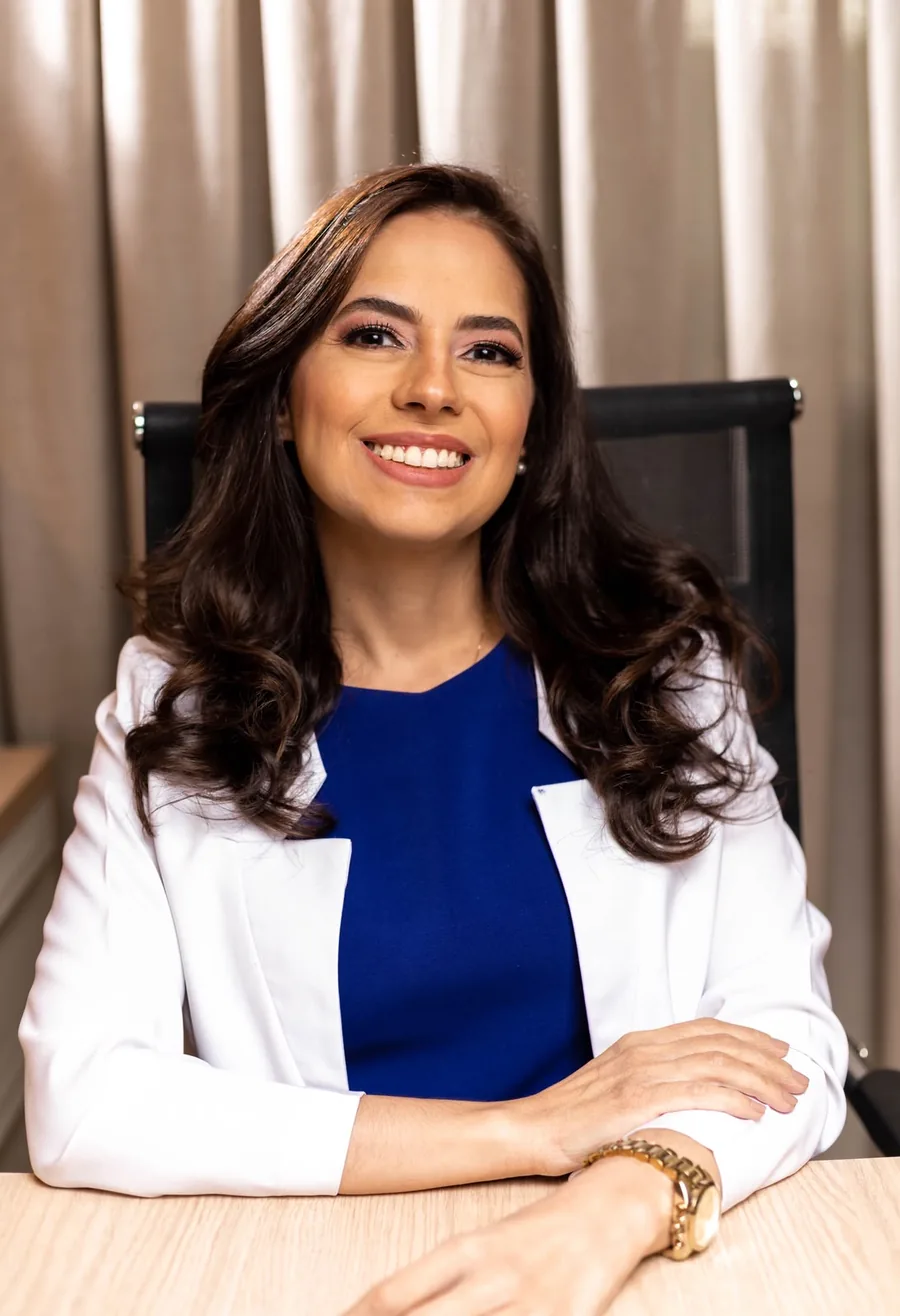 Dra. Fábia Gruppi, médica endocrinologista, sorrindo em sua mesa no consultório